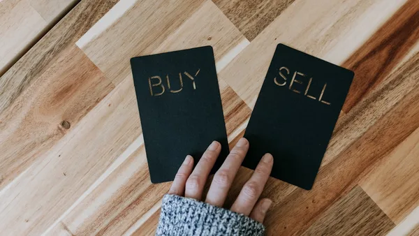 a person holding two small black books with the words buy and sell on them