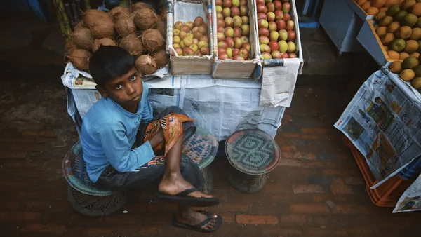Young boy sits near a fruit stand