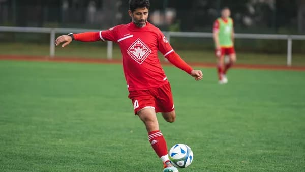 man in red soccer jersey kicking soccer ball on green grass field during daytime