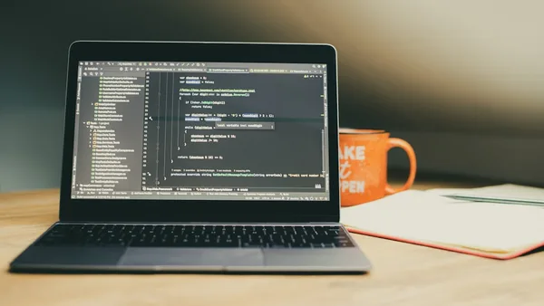 Laptop displaying code with an orange mug nearby