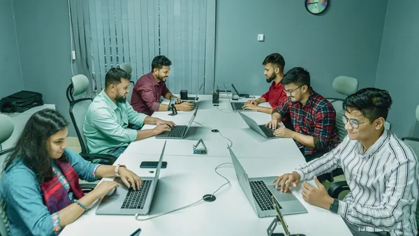 a group of people sitting around a table with laptops