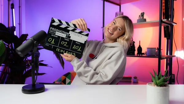 a woman sitting at a table holding a movie clapper