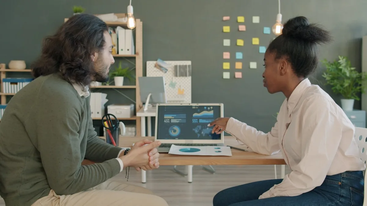 Two colleagues discussing data on a laptop screen.
