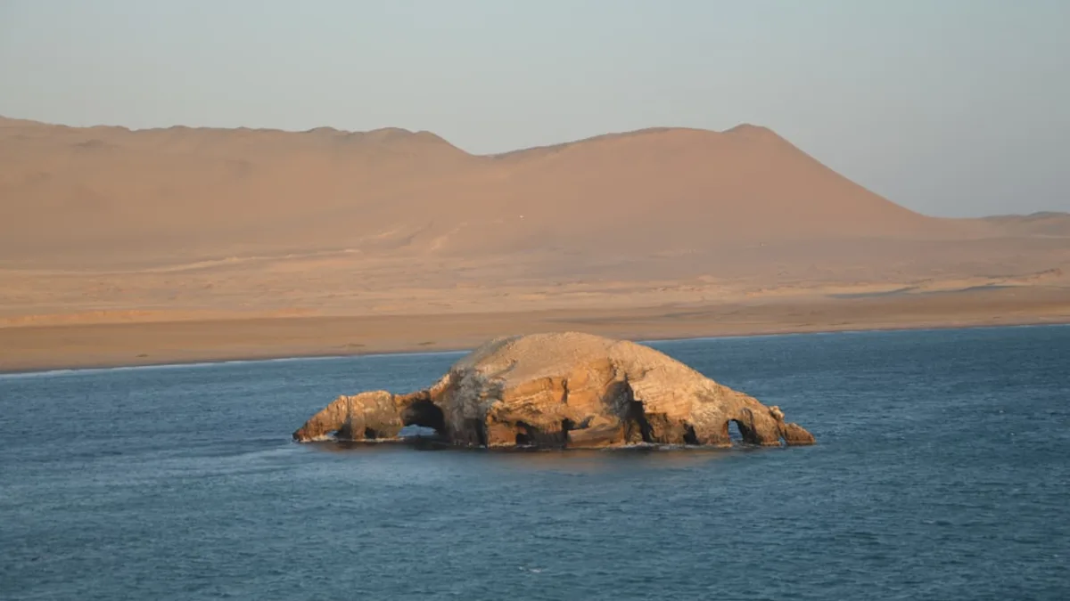 Rocky island with arch in blue ocean at sunset
