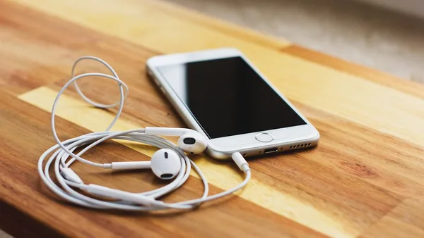 silver iPhone 6 with EarPods on brown wooden table