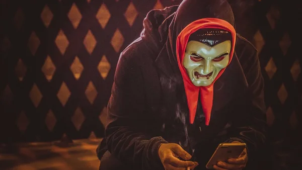 person in black and red mask holding smartphone