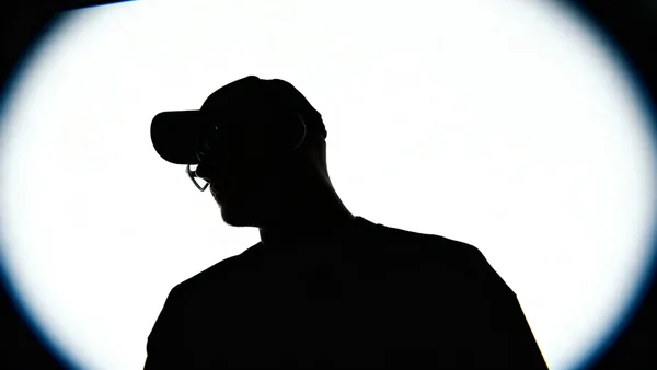 Silhouette of a person wearing a baseball cap and glasses.